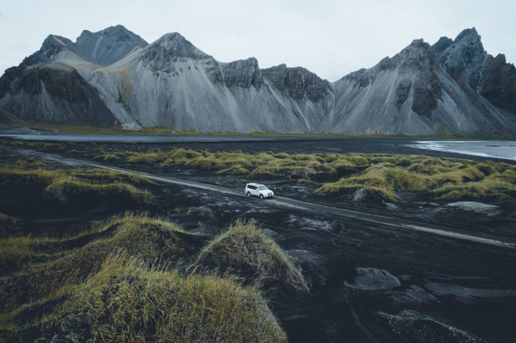 A white car traverses a gravel road against Iceland's dramatic mountain backdrop.